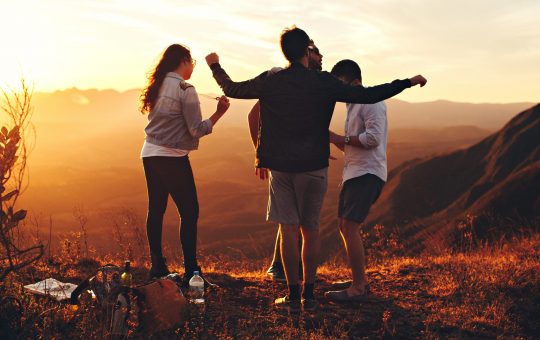 four-person-standing-at-top-of-grassy-mountain-697244